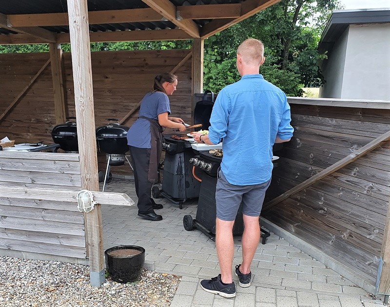 Forskellige grill under tag og grillmeister i gang med servere grillmad til ung mand