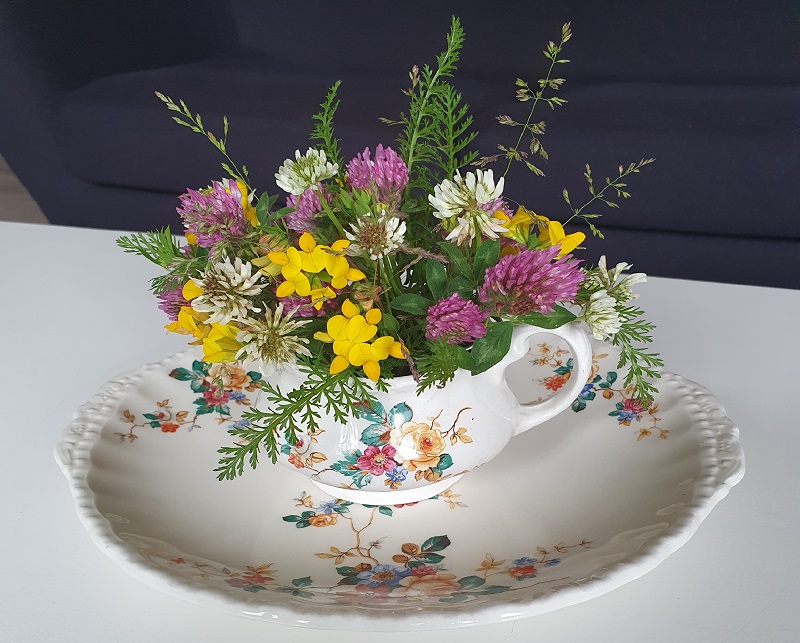 En gammel flødekande med et tilhørende rundt fad dekoreret med markens vilde blomster